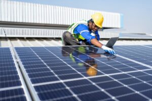 Engineer on rooftop sitting next to solar panels photo voltaic check laptop for installation